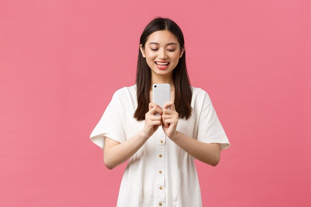 Beauté, émotions humaines et concept technologique. Une blogueuse asiatique souriante et heureuse, une fille élégante prenant une photo sur un smartphone, l'air optimiste en photographiant, prenant une photo avec un téléphone portable.