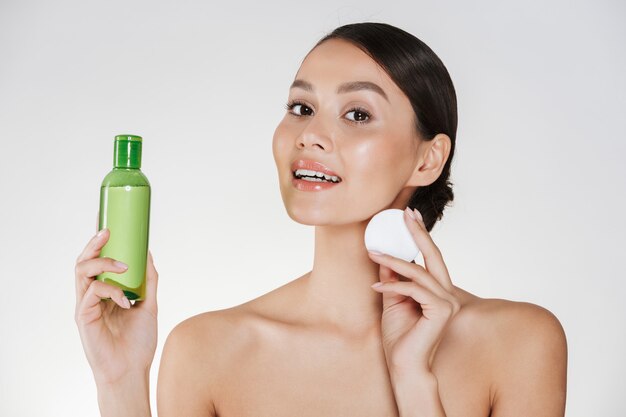 Beauté et hygiène matinale de jeune femme avec une peau douce et saine, nettoyage du visage avec de la lotion et du coton, isolé sur blanc