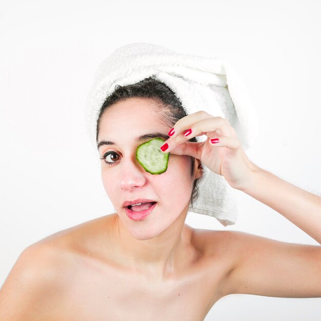 Beauté jeune femme avec une serviette enveloppée autour de la tête tenant une tranche de concombre sur ses yeux