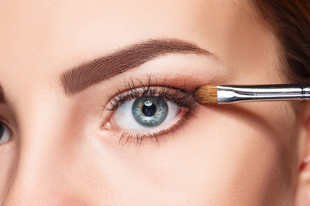 Beaux yeux féminins avec maquillage et pinceau sur blanc