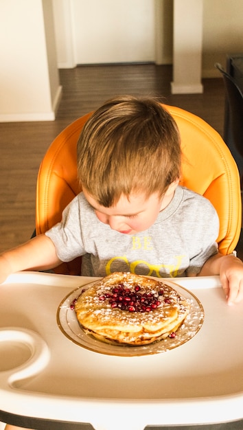 Bébé assis sur une chaise haute en regardant pancake sur une plaque