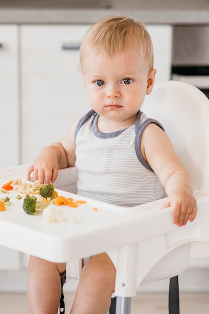 Bébé garçon en chaise haute manger des légumes dans la cuisine