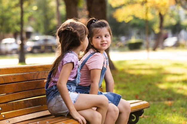 Photo gratuite bébé soeurs assis sur un banc à l'extérieur