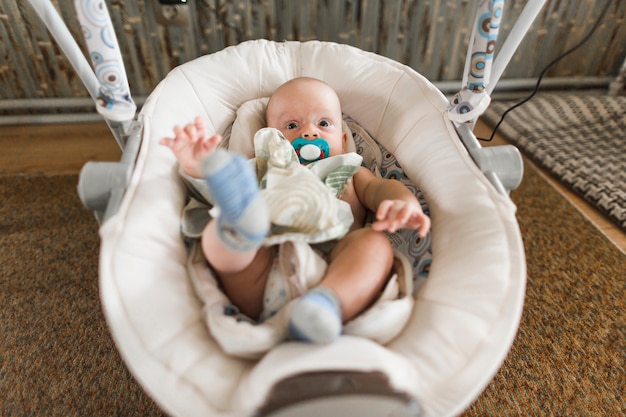 Bébé avec sucette allongé sur un landau à la maison