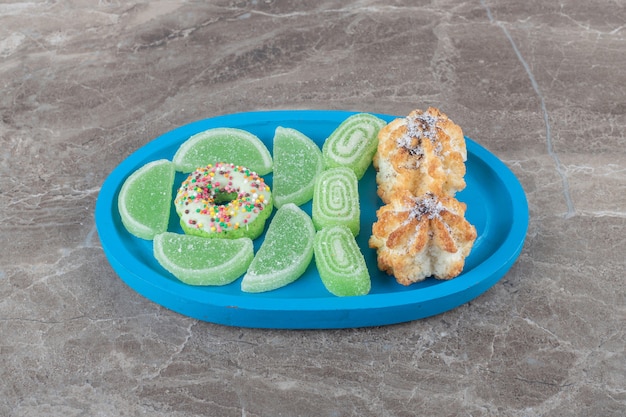Un beignet, des biscuits et des confitures sur un petit plateau sur une surface en marbre