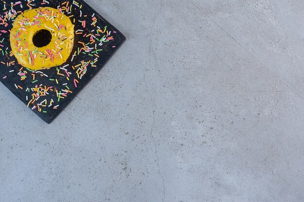 Beignet jaune simple décoré de pépites sur une planche à découper.