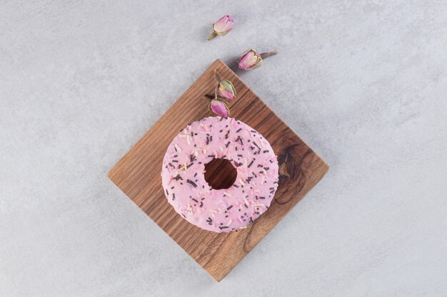 Beignet rose sucré décoré de paillettes sur planche de bois.