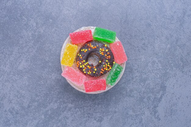 Beignet savoureux avec des bonbons à la gelée de fruits sur une surface grise