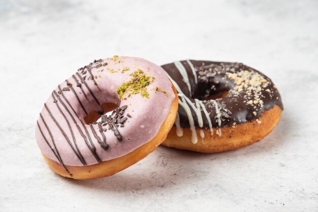 Beignets roses et chocolat avec des miettes de crème et de noix sur une surface blanche.