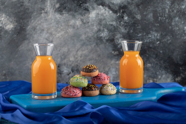 Beignets sucrés colorés avec des pots en verre de jus et une tasse de thé.