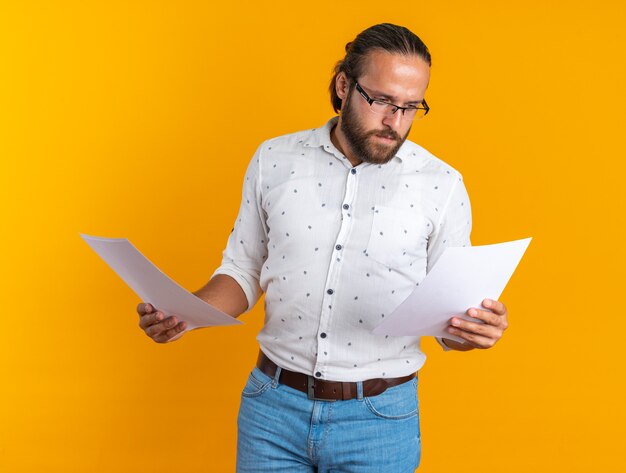 Bel homme adulte concentré portant des lunettes tenant des documents en regardant un