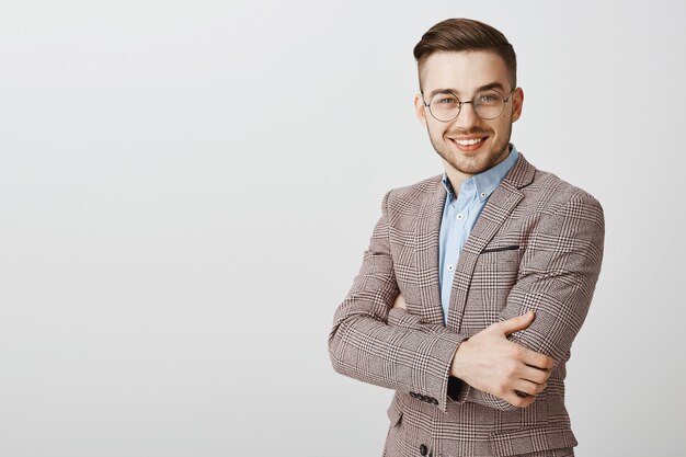 Bel homme d'affaires en costume et lunettes croise la poitrine des bras et regarde