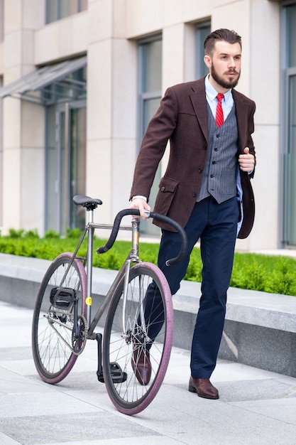 Bel homme d'affaires dans une veste et une cravate rouge et son vélo dans les rues de la ville.