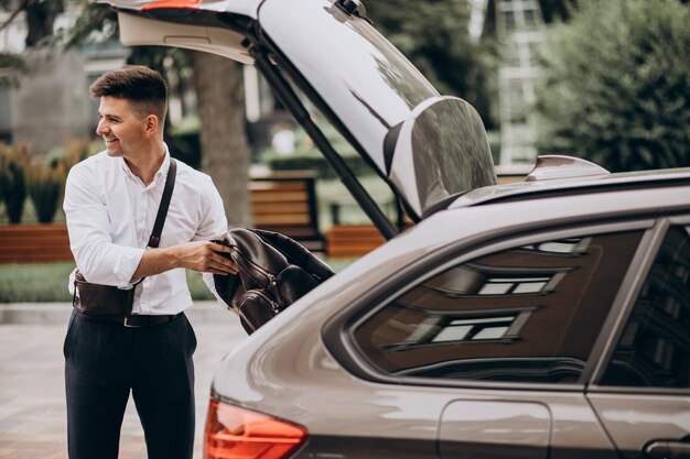 Bel homme d'affaires debout près de sa voiture lors d'un voyage d'affaires