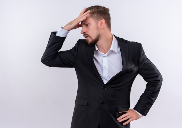 Bel homme d'affaires portant un costume à côté confus avec la main sur la tête debout sur fond blanc