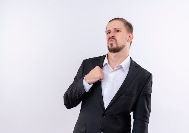 Bel homme d'affaires portant costume à côté avec une expression sceptique debout sur fond blanc