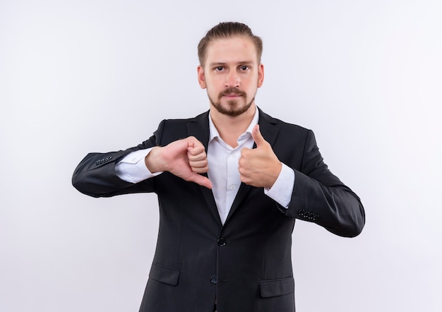 Bel homme d'affaires portant costume montrant les pouces de haut en bas debout sur fond blanc