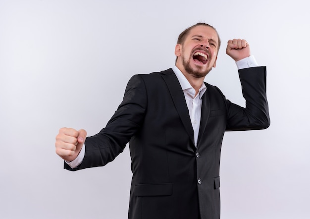 Bel homme d'affaires portant costume serrant les poings fou heureux debout sur fond blanc