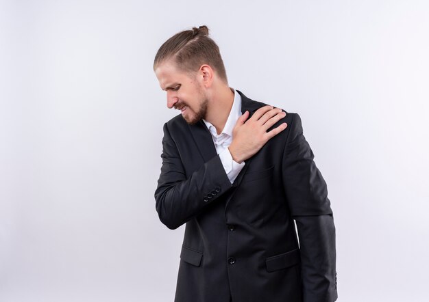 Bel homme d'affaires portant costume touchant l'épaule ressentant de la douleur debout sur fond blanc