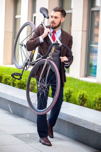 Bel homme d'affaires portant son vélo dans les rues de la ville. Le concept du mode de vie moderne des jeunes hommes