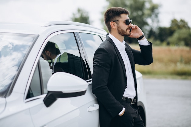 Bel homme d'affaires près de la voiture blanche