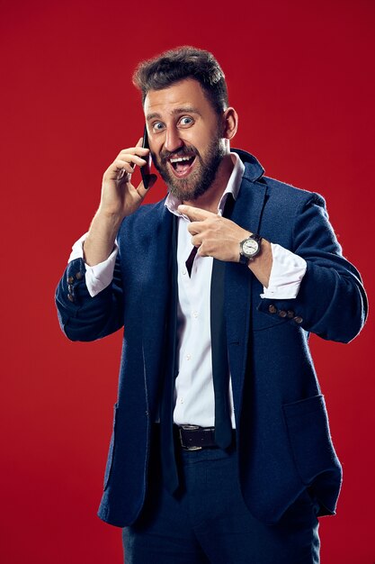 Bel homme d'affaires avec téléphone mobile. Homme d'affaires heureux debout isolé sur rouge. Beau portrait mâle demi-longueur