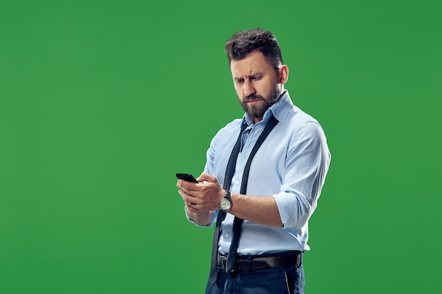 Bel homme d'affaires vérifiant les e-mails sur le téléphone. Homme d'affaires sérieux debout isolé sur vert. Beau portrait mâle demi-longueur