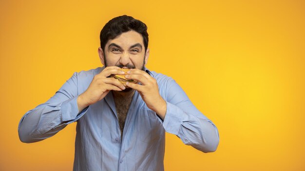 Un bel homme affamé tient un hamburger à la main sur fond jaune