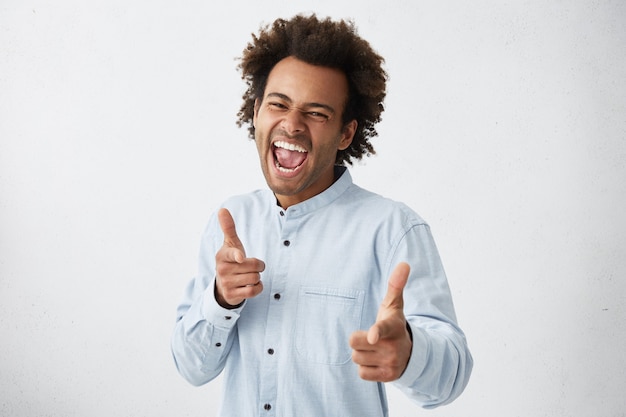 Photo gratuite bel homme afro-américain en chemise blanche avec plein de bonheur pointant l'index