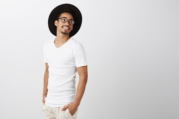 Bel homme afro-américain élégant dans des verres et un chapeau hipster à droite avec un sourire heureux