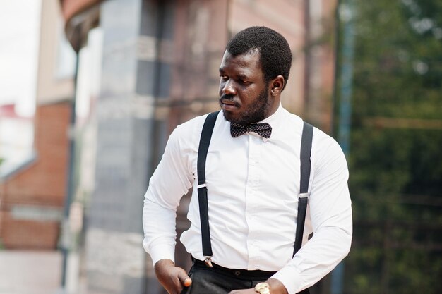 Bel homme afro-américain à la mode en tenue de soirée noeud papillon et bretelles bâton de marche