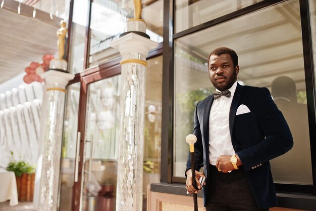 Bel homme afro-américain à la mode en tenue de soirée et noeud papillon avec canne