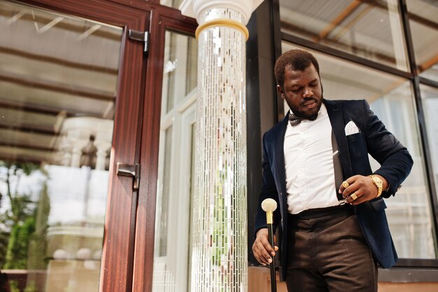 Bel homme afro-américain à la mode en tenue de soirée et noeud papillon avec canne