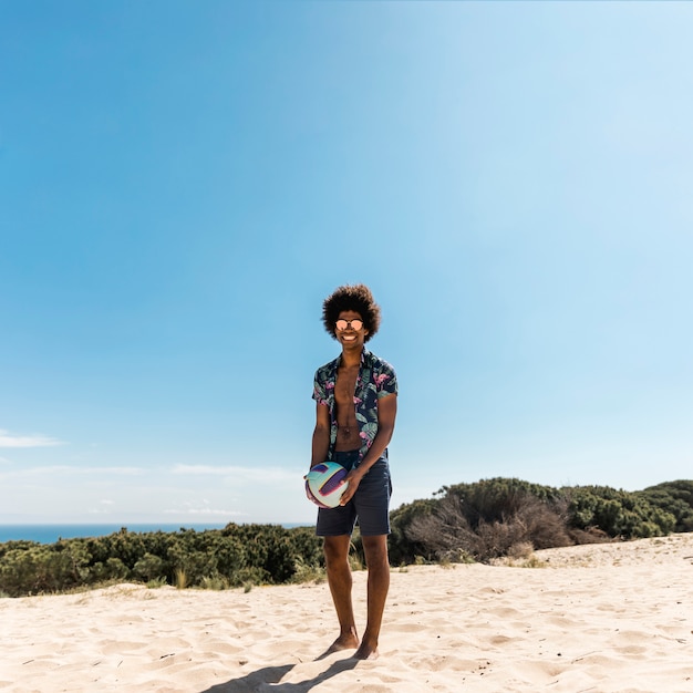 Bel homme afro-américain posant avec ballon sur la plage