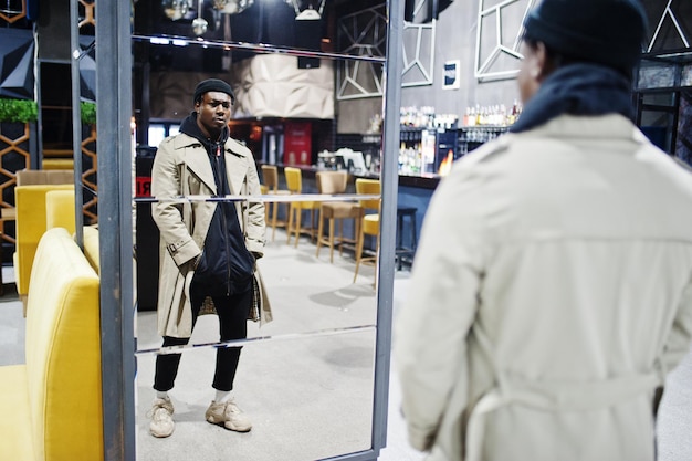 Bel homme afro-américain posant à l'intérieur de la boîte de nuit en chapeau noir et manteau beige