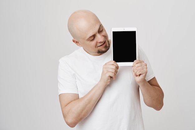 Bel homme d'âge moyen chauve montrant l'écran de la tablette numérique