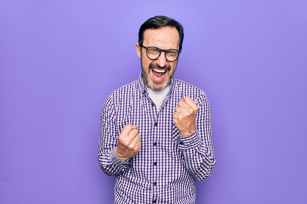 Photo gratuite bel homme d'âge moyen portant une chemise décontractée et des lunettes sur fond blanc isolé célébrant la surprise et l'émerveillement du succès avec les bras levés et les yeux fermés