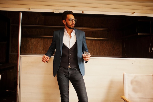 Photo gratuite bel homme arabe bien habillé fume un cigare avec un verre de whisky au balcon du pub