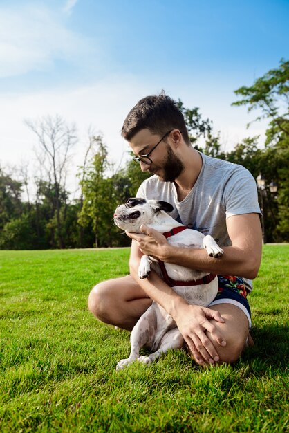 Bel homme assis avec un bouledogue français sur l'herbe dans le parc