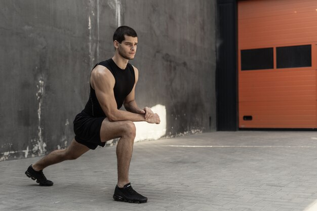 Bel homme athlétique s'échauffant qui s'étend avant l'entraînement