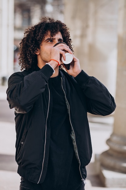 Bel homme aux cheveux bouclés, boire du café dans la rue