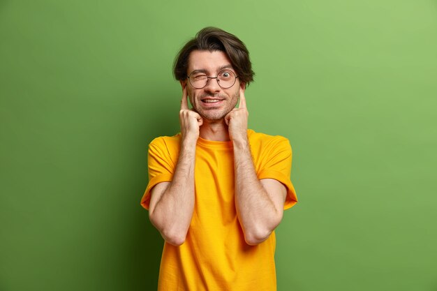 Bel homme aux cheveux noirs se bouche les oreilles cligne de l'œil évite le son fort