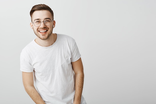 Bel homme aux dents blanches, souriant et portant des lunettes sur un mur gris