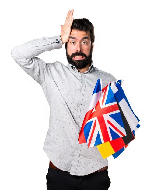 Bel homme à la barbe tenant de nombreux drapeaux et ayant des doutes