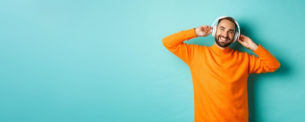 Photo gratuite bel homme barbu écoutant de la musique dans des écouteurs souriant heureux debout sur zone turquoise