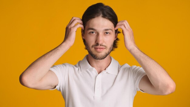 Bel homme barbu regardant confiant fixant ses cheveux et regardant la caméra sur fond coloré Modèle masculin posant en studio