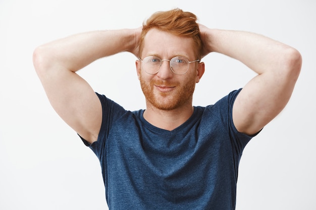 Bel homme barbu rousse impertinent dans des verres, tenant les mains derrière la tête détendue, au repos