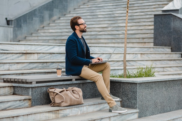 Bel homme barbu souriant dans des verres travaillant sur ordinateur portable