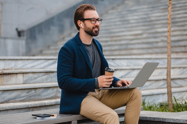 Bel homme barbu souriant dans des verres travaillant sur ordinateur portable