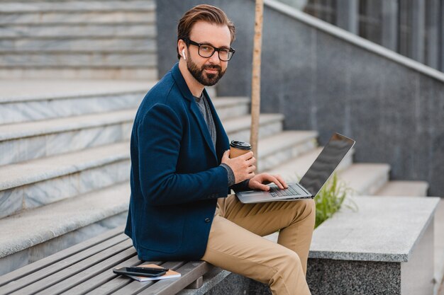 Bel homme barbu souriant dans des verres travaillant sur ordinateur portable